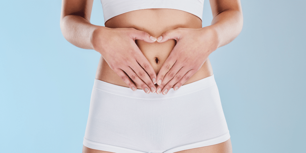 Your clients shouldn't reverse diet if they have gut health issues. Woman in white shorts and sports bra holding her hands over her stomach in the shape of a heart.