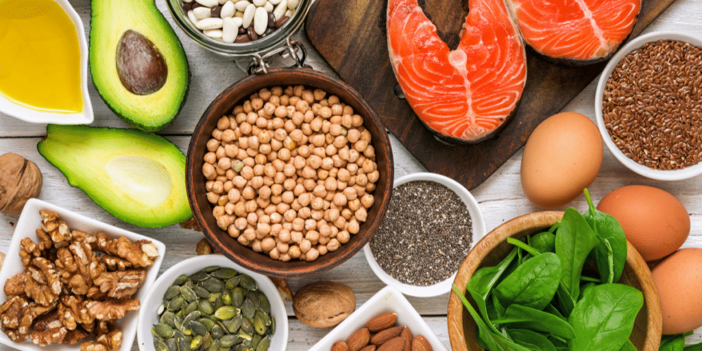 Adequate sleep plays an important role in health outcomes. Table full of healthy foods like chickpeas, walnuts, beans, pumpkin seeds, eggs, salmon, and avocado.